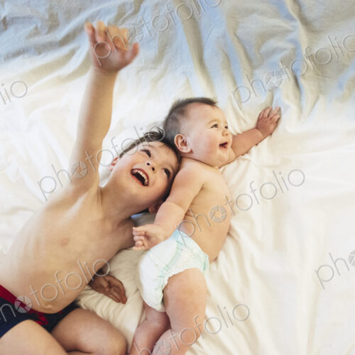Two children, a brother and baby sister lying down playing together.
