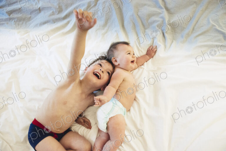Two children, a brother and baby sister lying down playing together.