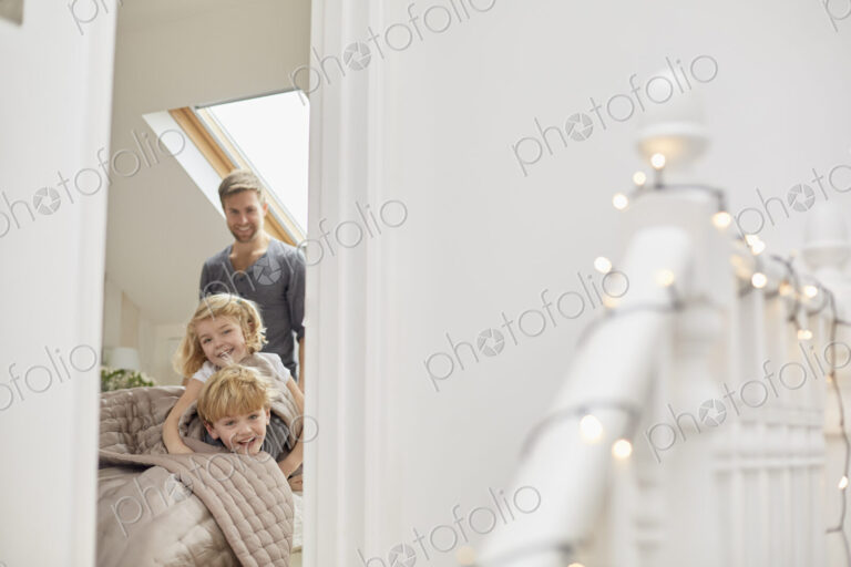 Two children and a man in a bedroom looking excitedly through the door.