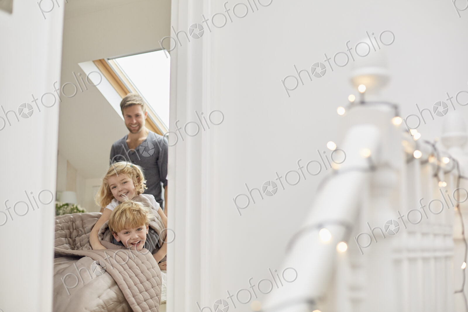 Two children and a man in a bedroom looking excitedly through the door.