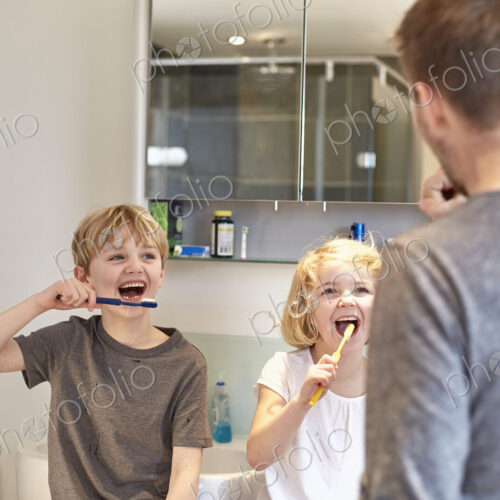 Two children and an adult man cleaning their teeth with toothbrushes in a bathroom. Two children and an adult man cleaning their teeth with toothbrushes in a bathroom.