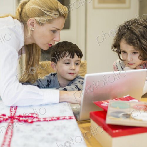 Two children and their mother looking at a laptop computer screen around a kitchen table. Two children and their mother looking at a laptop computer screen around a kitchen table.