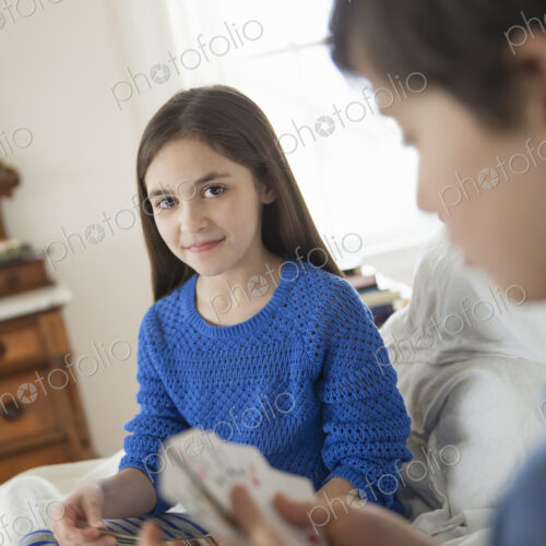 Two children at home, sitting side by side and playing a game of cards.