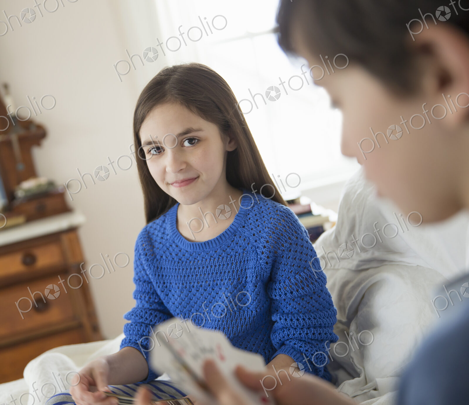Two children at home, sitting side by side and playing a game of cards.