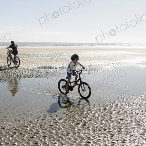 Two children cycling on an open beach, a boy and girl.