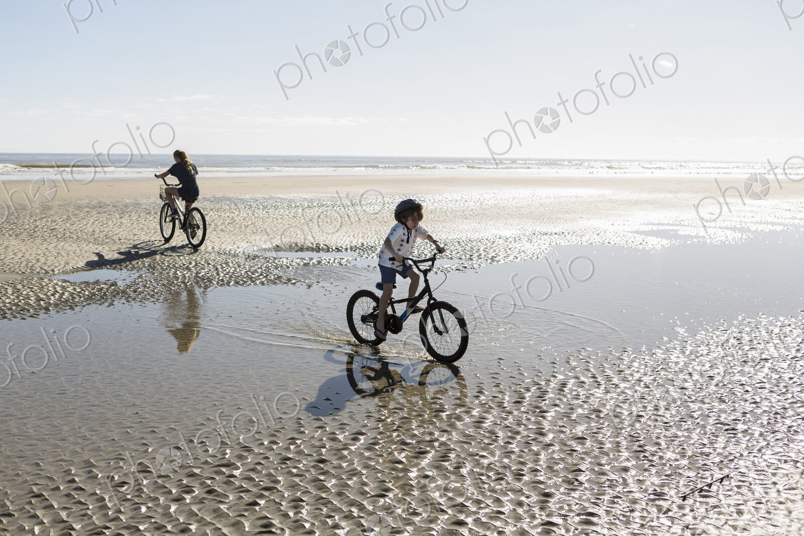 Two children cycling on an open beach, a boy and girl.