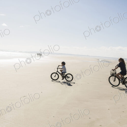 Two children cycling on an open beach, a boy and girl.