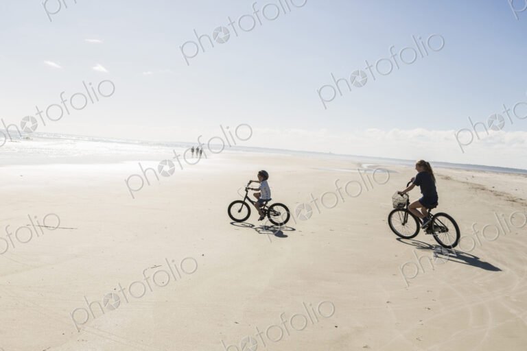 Two children cycling on an open beach, a boy and girl.