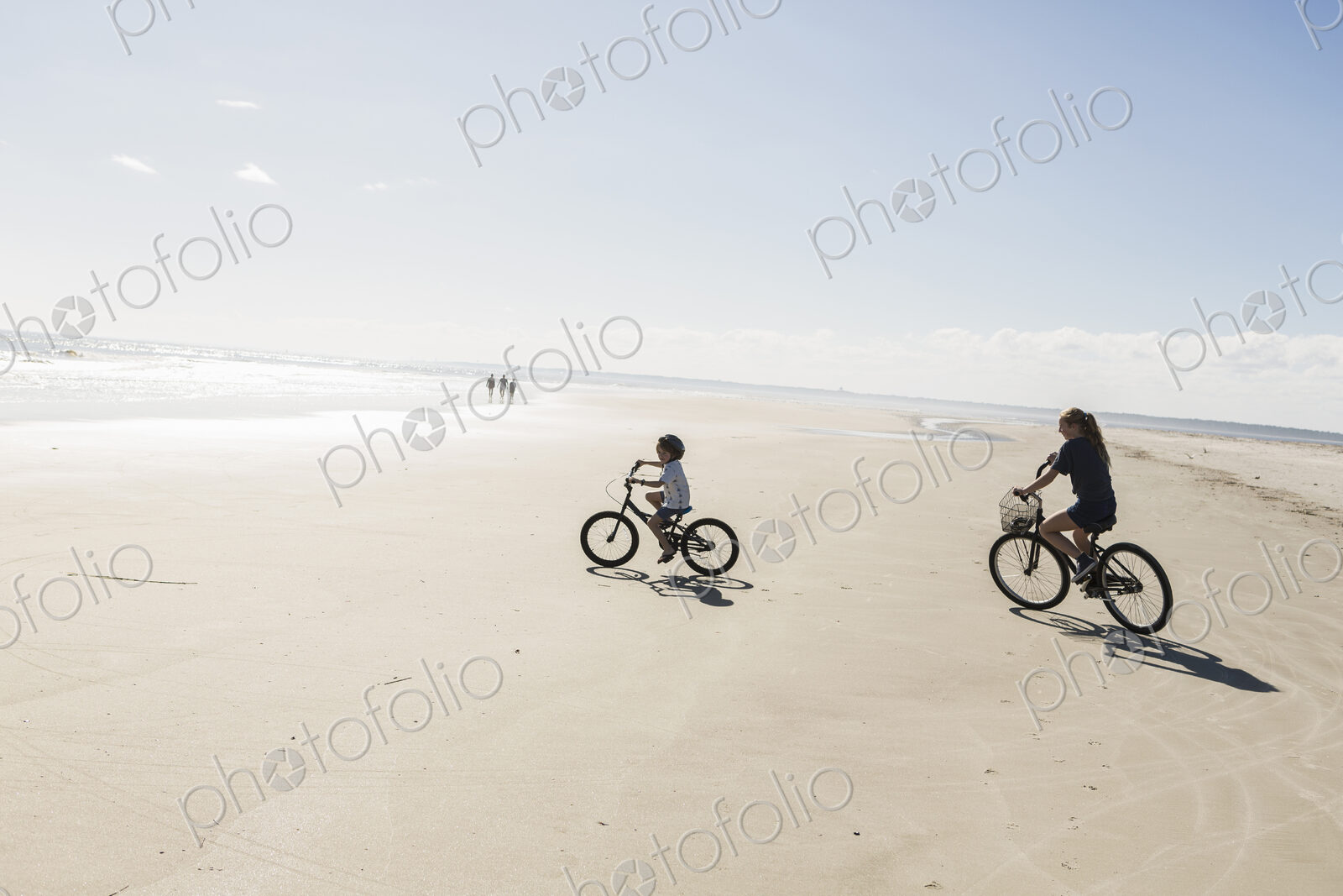 Two children cycling on an open beach, a boy and girl.