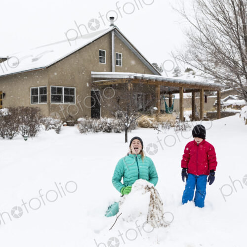 Two children in snow suits outdoors building a snowman Two children in snow suits outdoors building a snowman