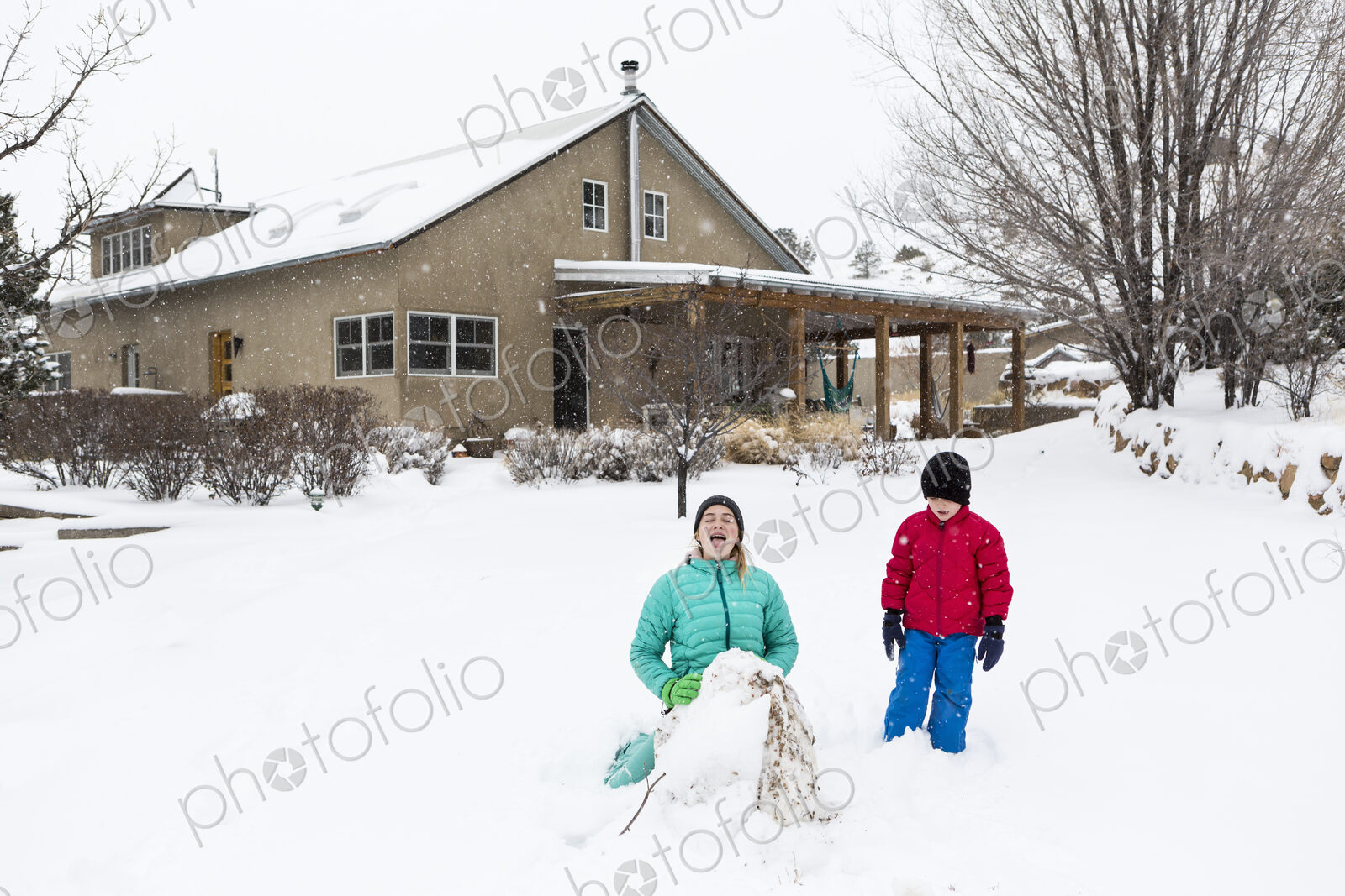 Two children in snow suits outdoors building a snowman