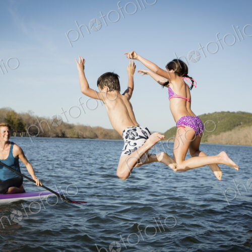 Two children leaping into the water from a jetty.