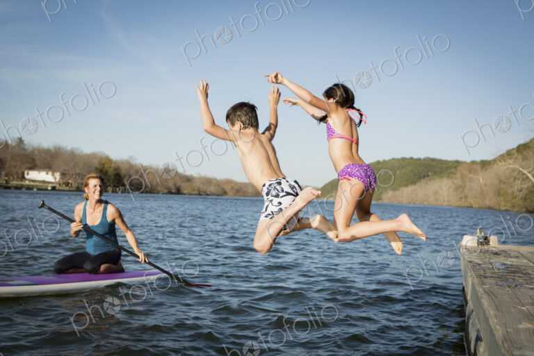 Two children leaping into the water from a jetty.