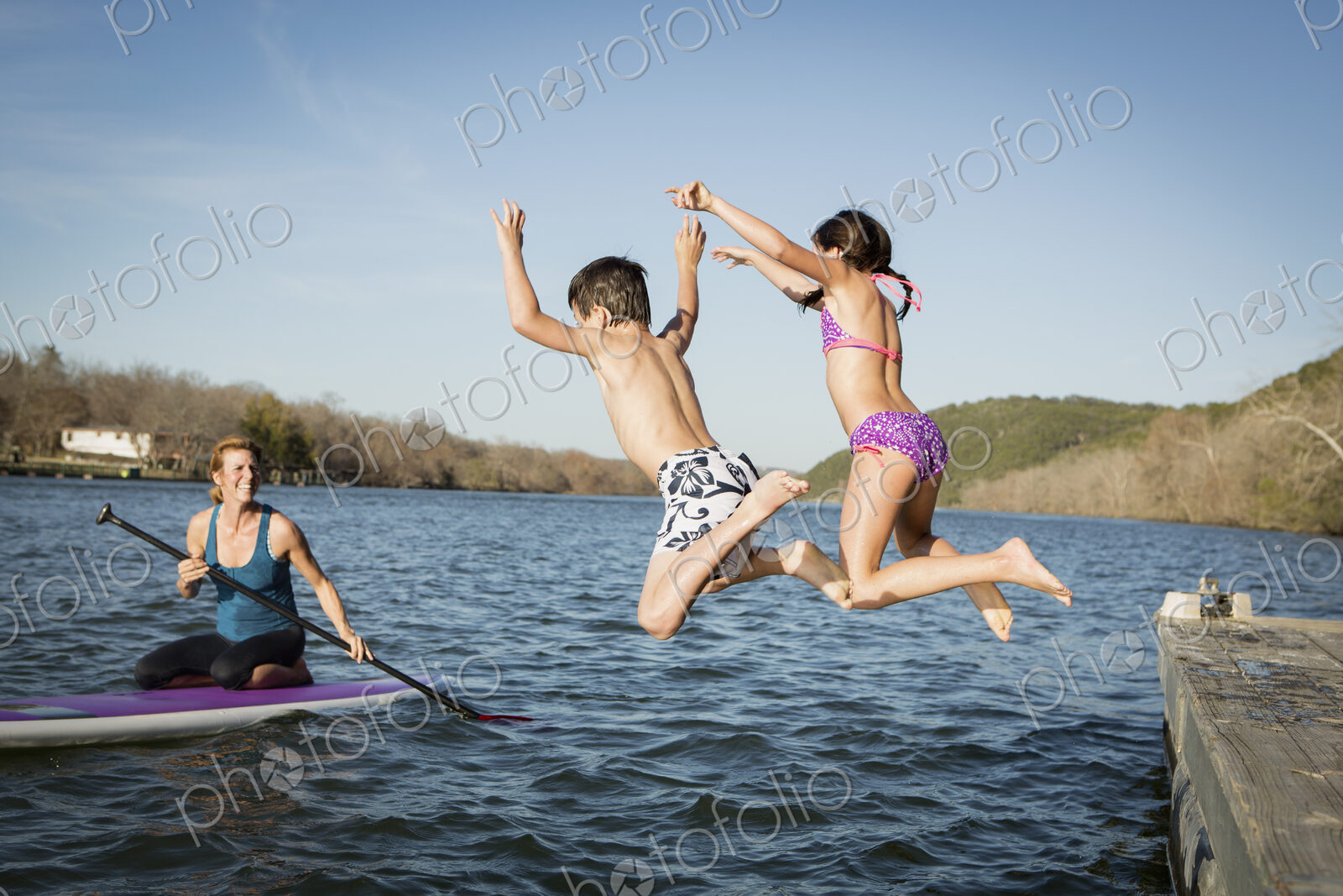Two children leaping into the water from a jetty.