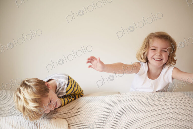 Two children playing behind a sofa, a boy and girl laughing.