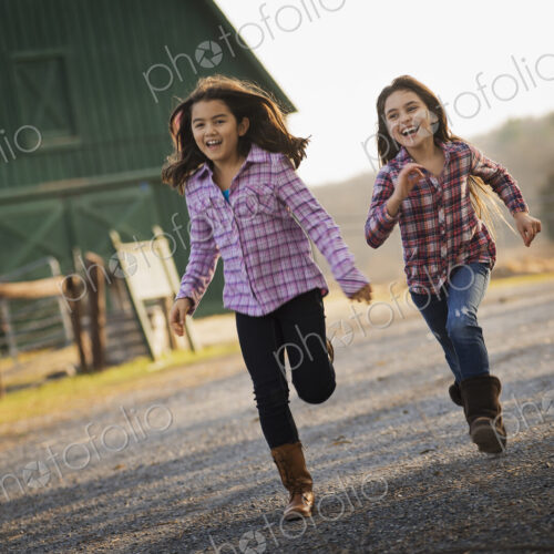 Two children running along a road, by a farm building, on an organic farm.