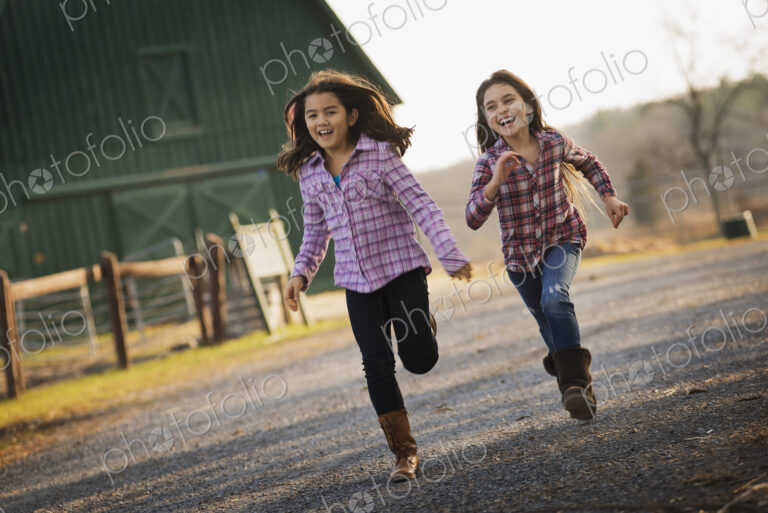 Two children running along a road, by a farm building, on an organic farm.