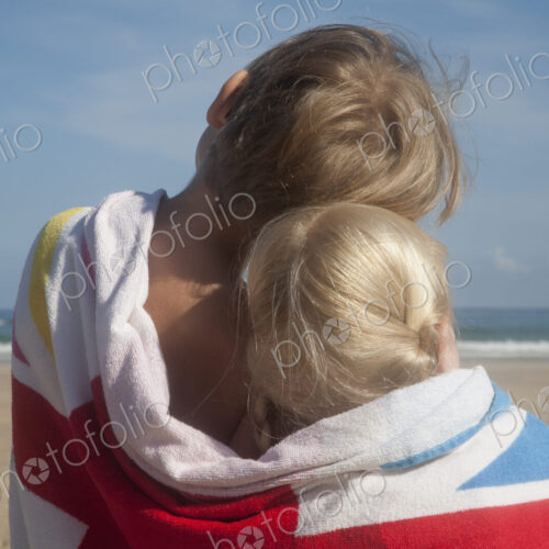 Two children sharing a towel. Back view of a brother and sister sitting on the beach… Two children sharing a towel. Back view of a brother and sister sitting on the beach…