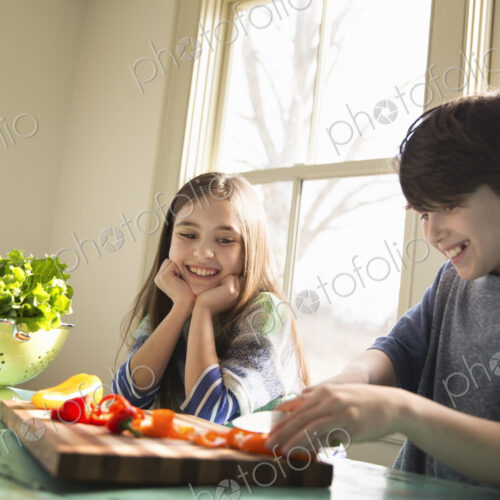 Two children sitting at a table. A boy using a knife and chopping bell peppers on a board. Two children sitting at a table. A boy using a knife and chopping bell peppers on a board.