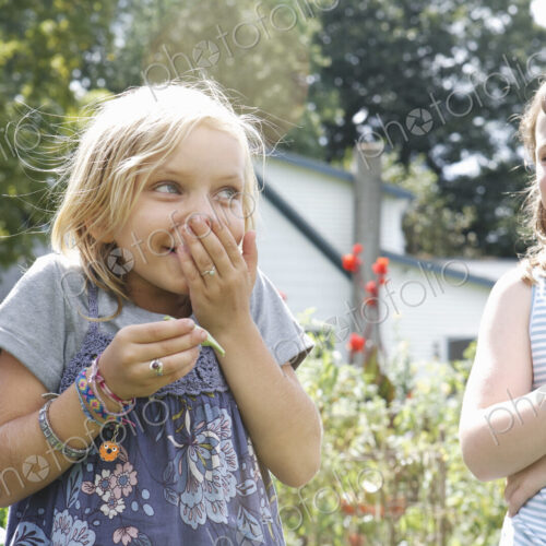 Two children standing outdoors in a garden laughing. Two children standing outdoors in a garden laughing.