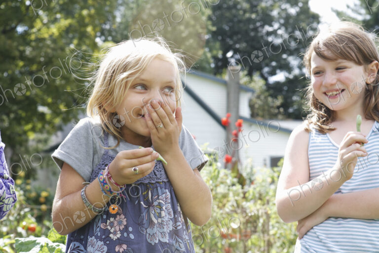 Two children standing outdoors in a garden laughing.