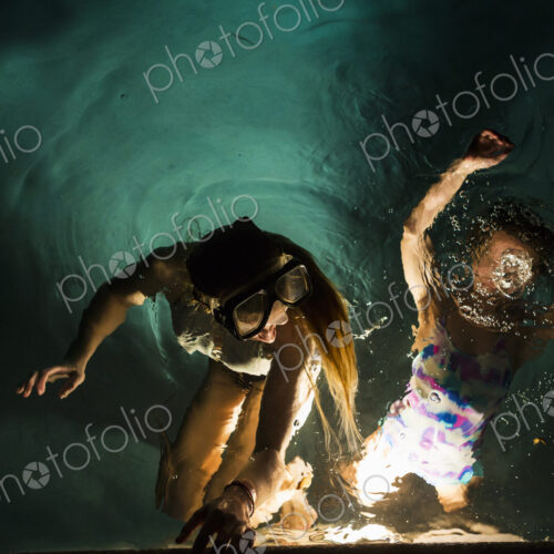 Two children swimming in pool at night Two children swimming in pool at night