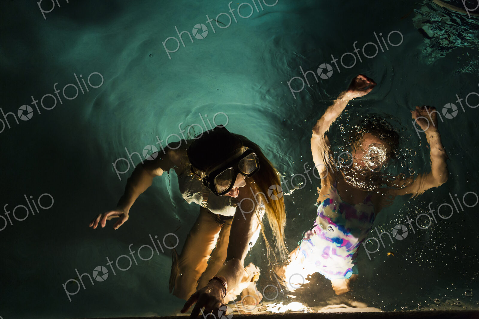 Two children swimming in pool at night