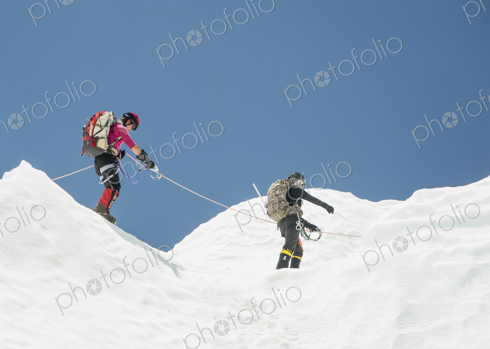 Two climbers in snow on a mountain, roped together.