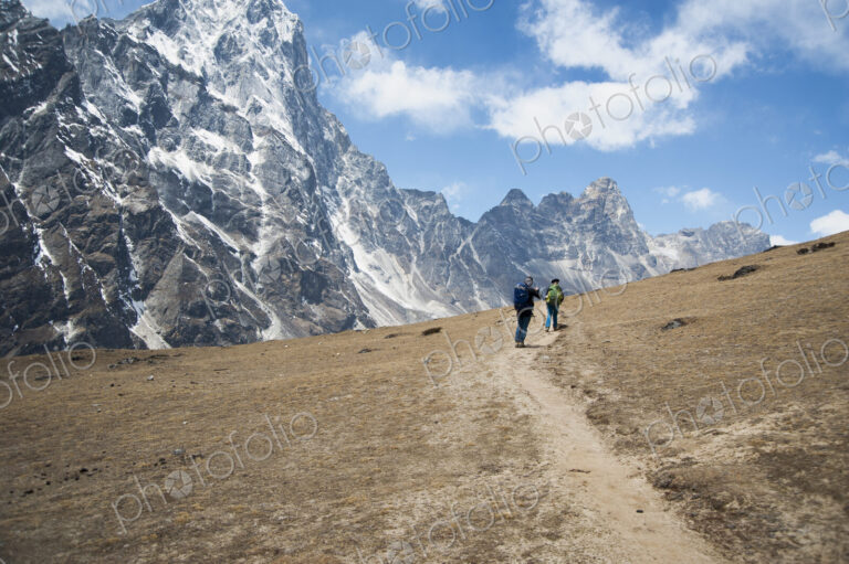 Two climbers on a path facing the steep mountains.