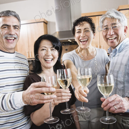 Two couples in a kitchen, Asian and Caucasian men and women making a toast with…
