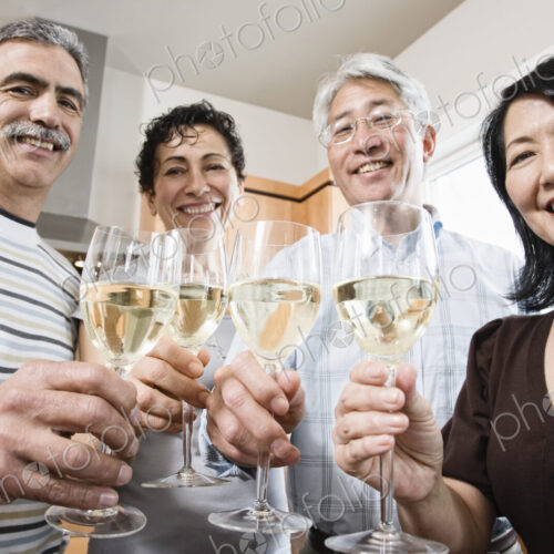 Two couples in a kitchen, Asian and Caucasian men and women making a toast with…