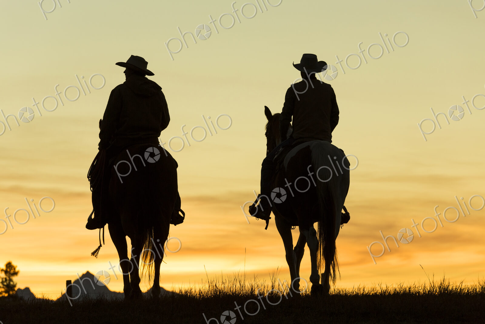 Two cowboys riding on horseback in a Prairie landscape at sunset.