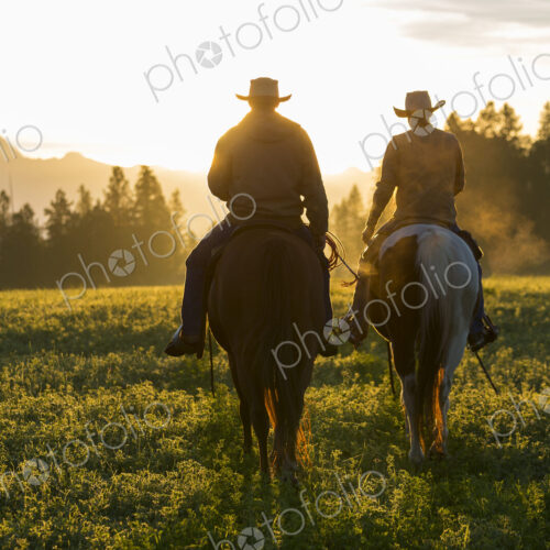 Two cowboys riding on horseback in a Prairie landscape at sunset. Two cowboys riding on horseback in a Prairie landscape at sunset.