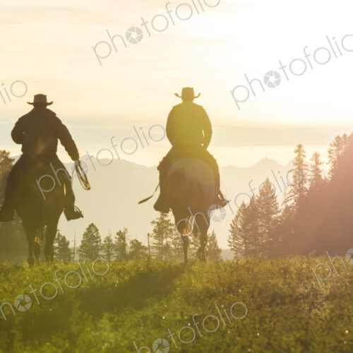 Two cowboys riding on horseback in a Prairie landscape at sunset. Two cowboys riding on horseback in a Prairie landscape at sunset.