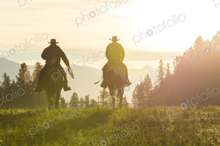 Two cowboys riding on horseback in a Prairie landscape at sunset.