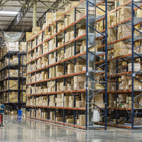 Two employees checking inventory beside racks of boxes in temporary storage in a… Two employees checking inventory beside racks of boxes in temporary storage in a…