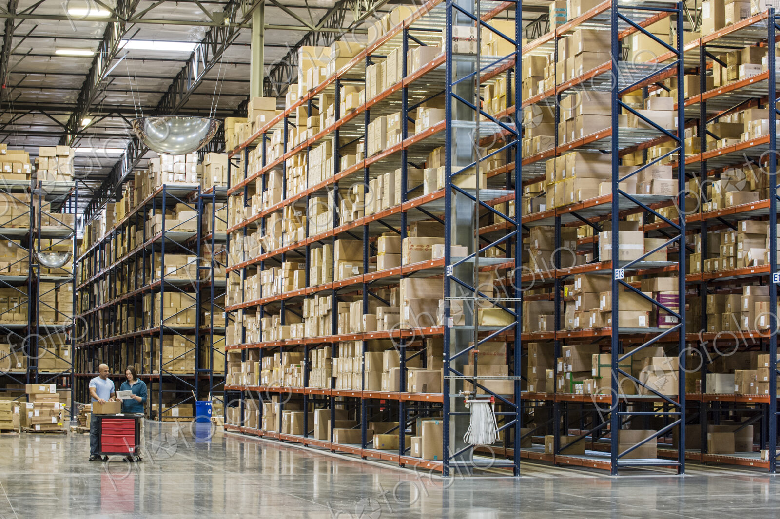 Two employees checking inventory beside racks of boxes in temporary storage in a…