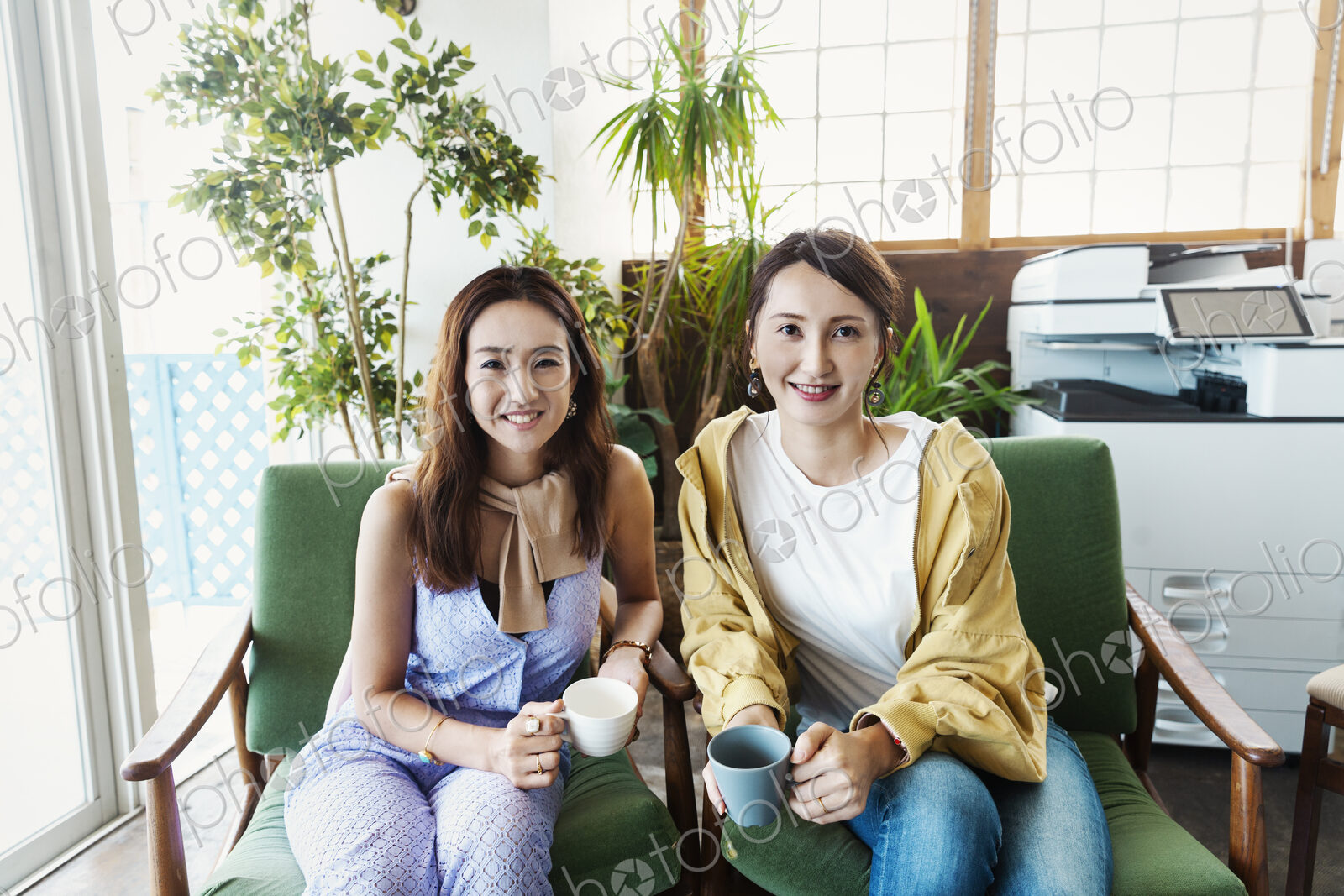 Two female Japanese professionals sitting in a co-working space, smiling at camera.