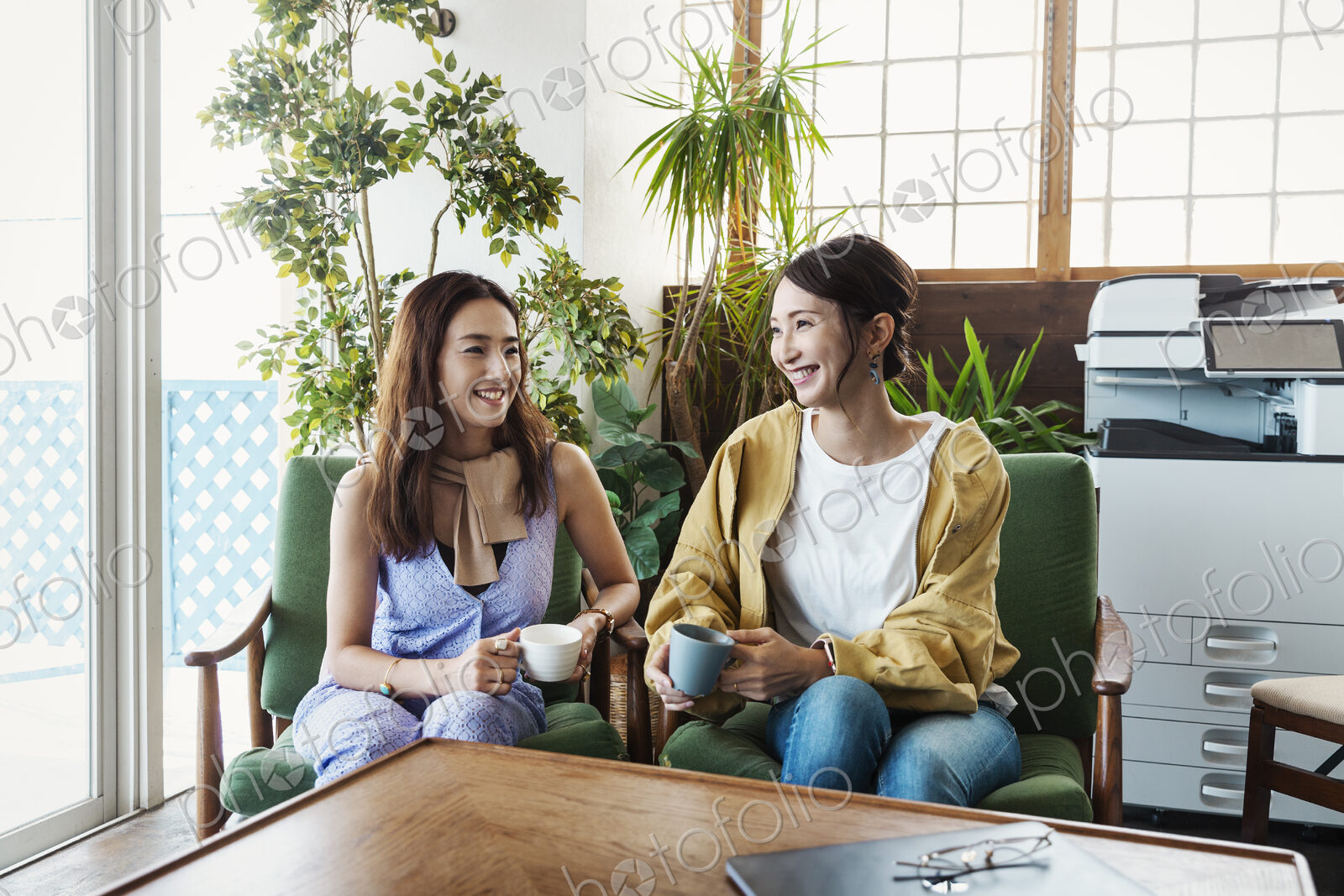 Two female Japanese professionals sitting in a co-working space, smiling at each other.