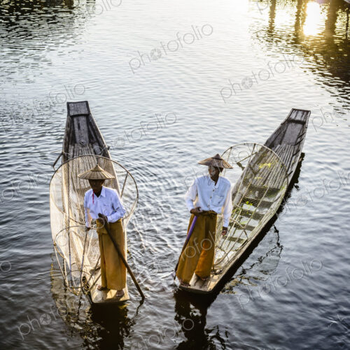 Two fishermen on traditional boats on the lake with fishing nets.