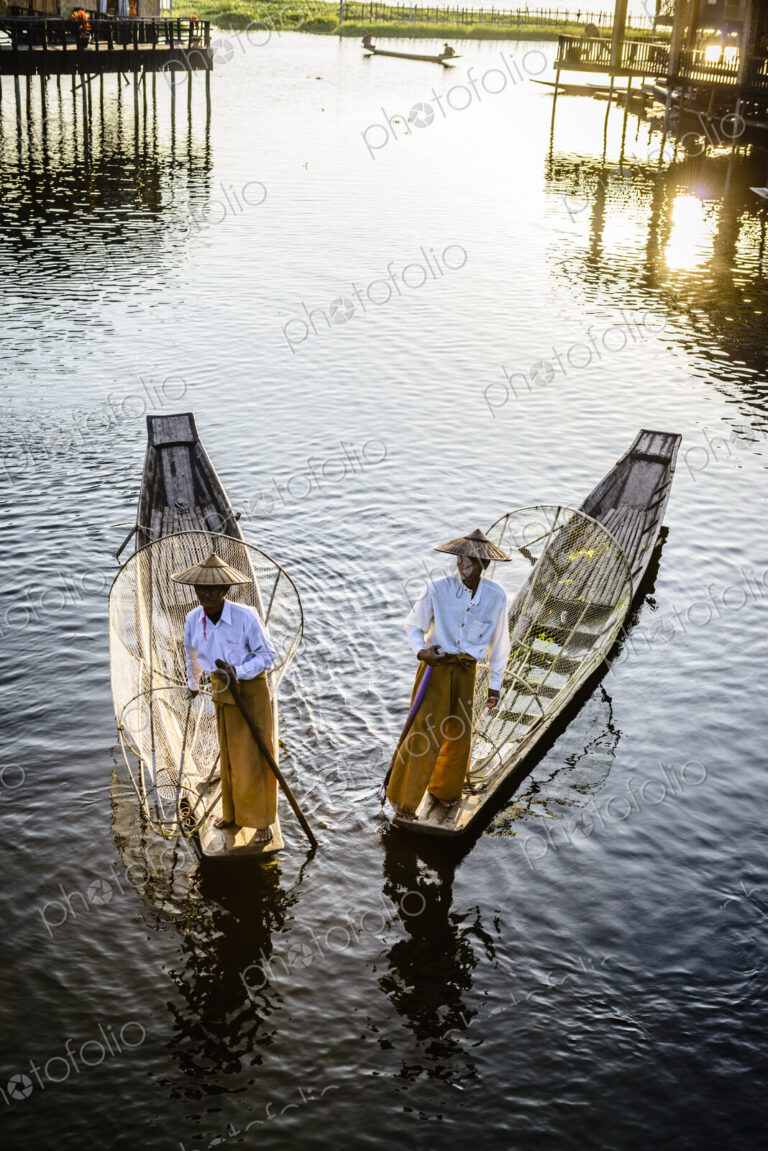 Two fishermen on traditional boats on the lake with fishing nets.