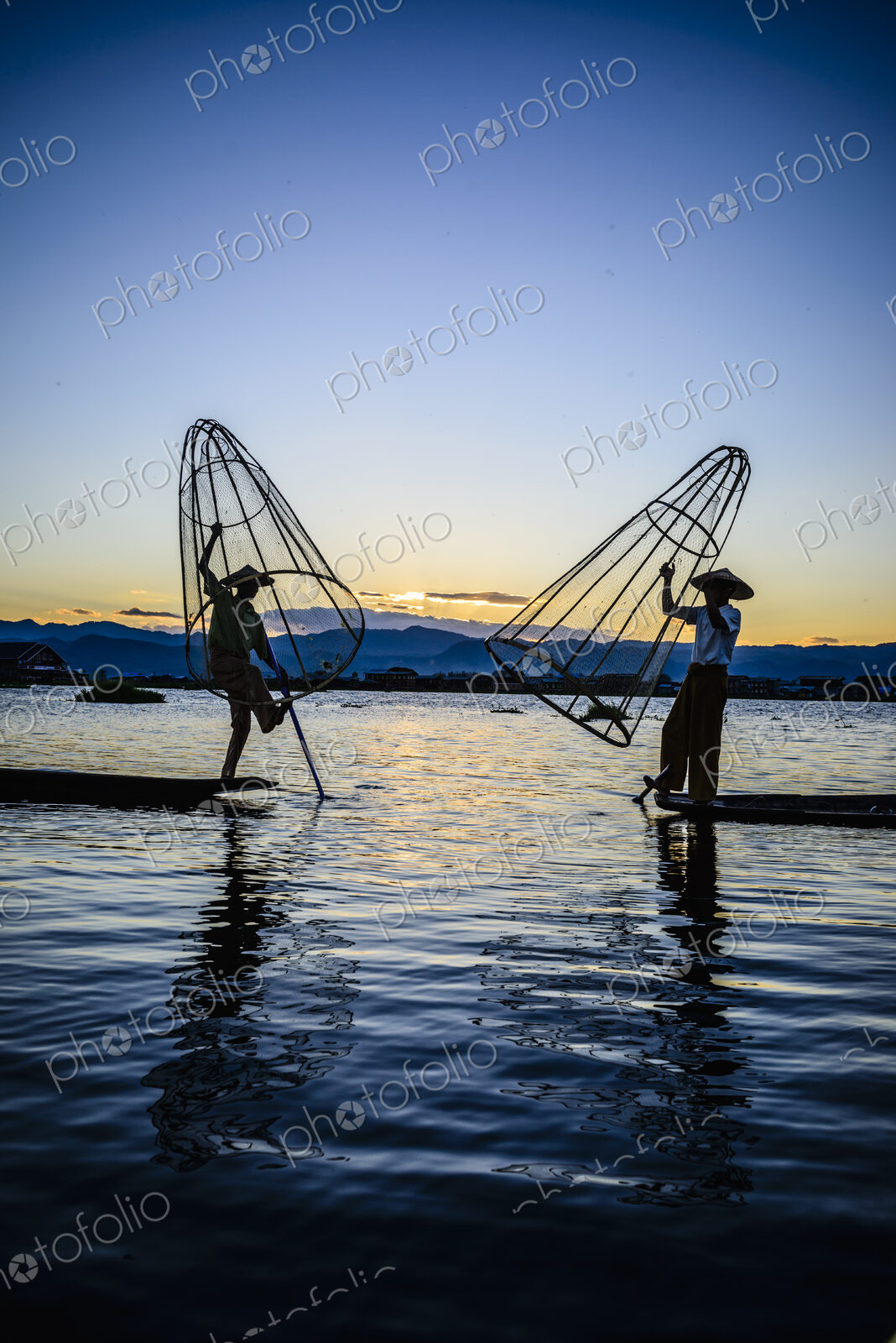 Two fishermen standing on their boats fishing on Lake Inle at dusk.