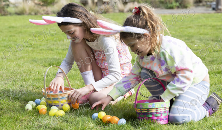 Two girls collecting Easter eggs in garden.