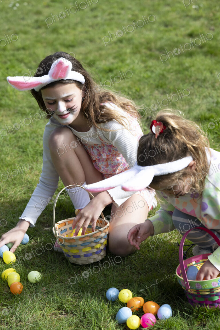 Two girls collecting Easter eggs in garden.