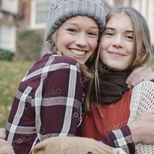 Two girls in hats and gloves wrapped up for cold weather, hugging and laughing. Two girls in hats and gloves wrapped up for cold weather, hugging and laughing.