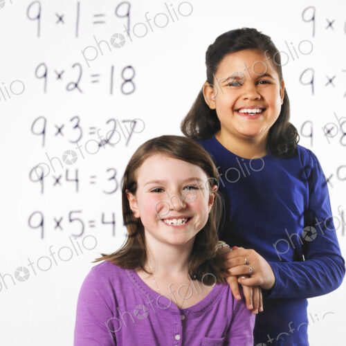 Two girls looking at a series of mathematical multiplication tables on a see through…