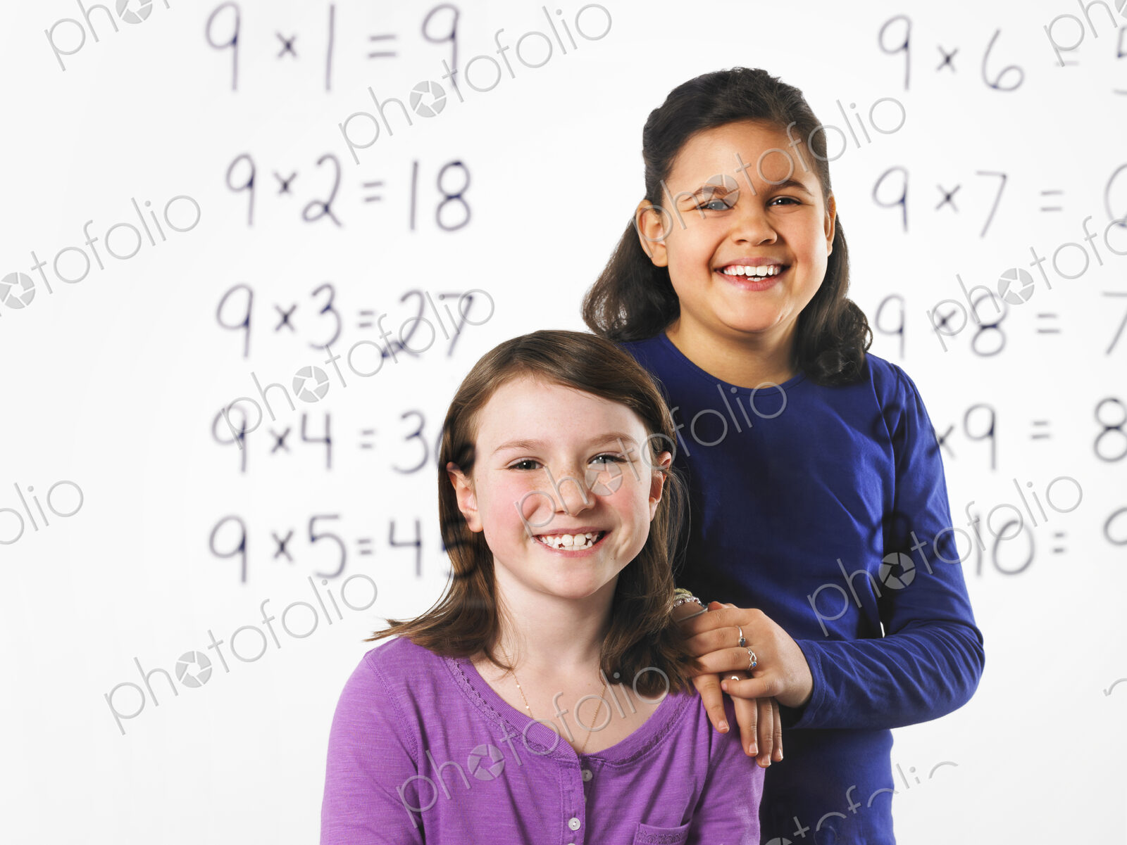 Two girls looking at a series of mathematical multiplication tables on a see through…