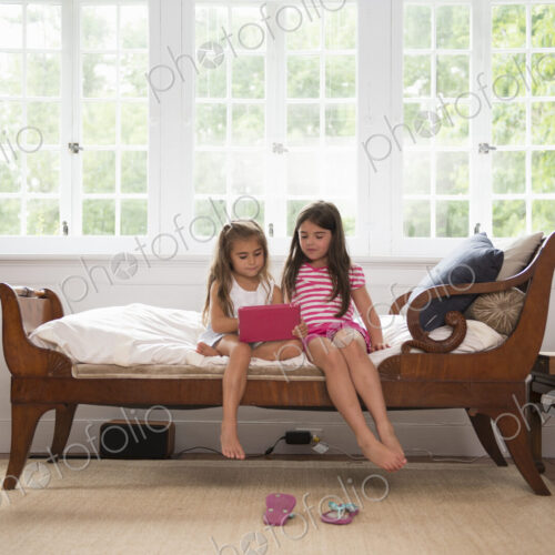 Two girls playing indoors, looking at a digital tablet.