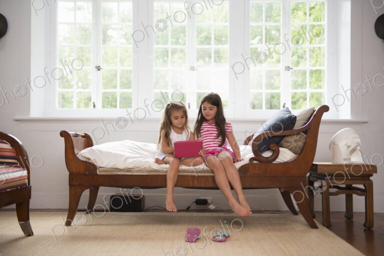 Two girls playing indoors, looking at a digital tablet.