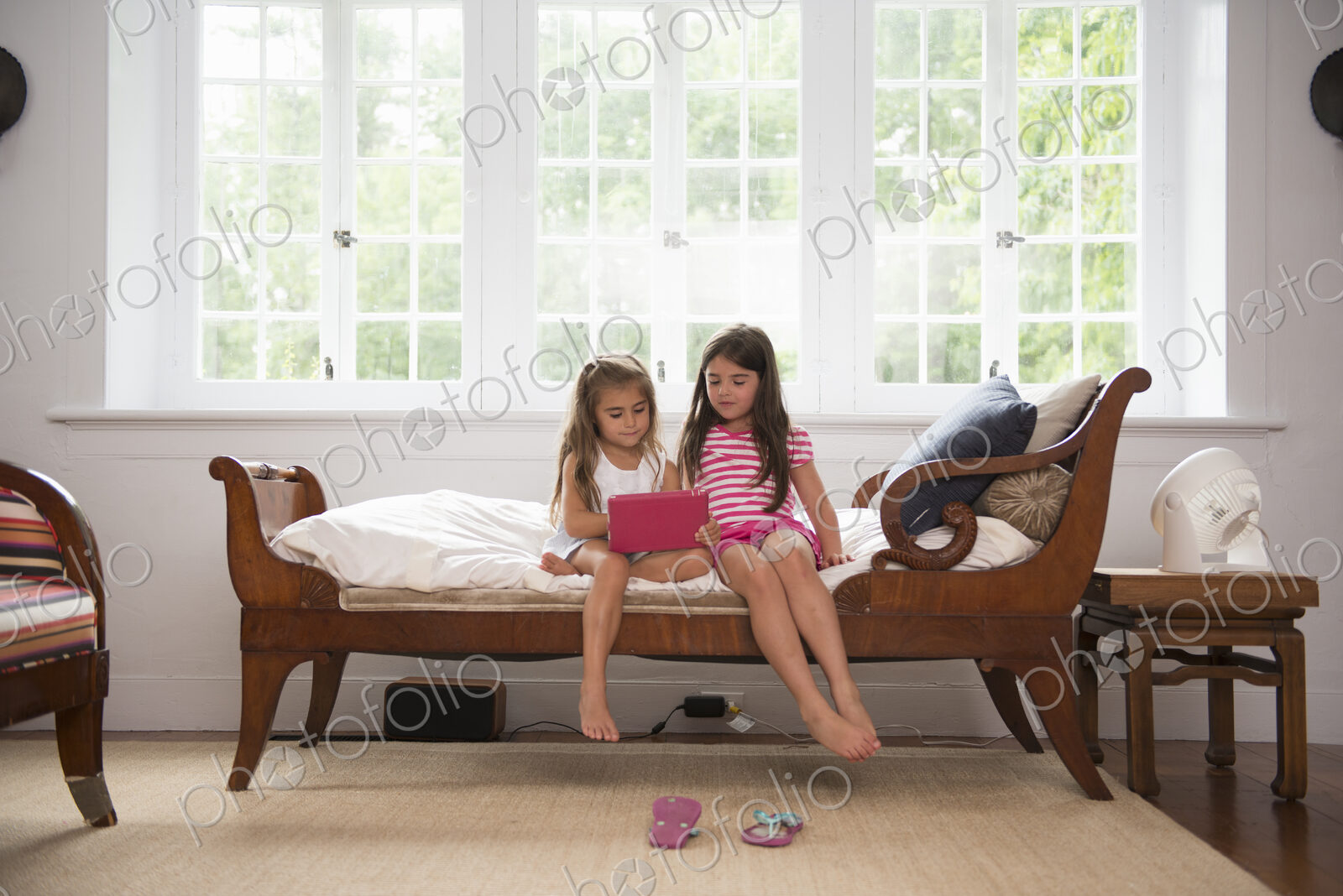 Two girls playing indoors, looking at a digital tablet.
